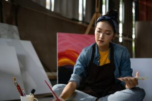 Aziatische vrouwelijke kunstenares tekent kunststukje met palet en penseel schilderen in atelier