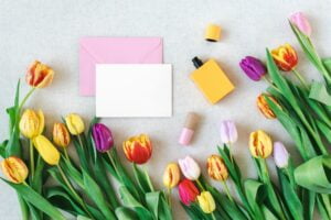 Colorful spring mockup of bright tulips, perfume, and postcard on a neutral background.