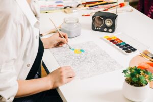 Young woman coloring page antistress at table indoors, mental wellbeing and arts-based therapy