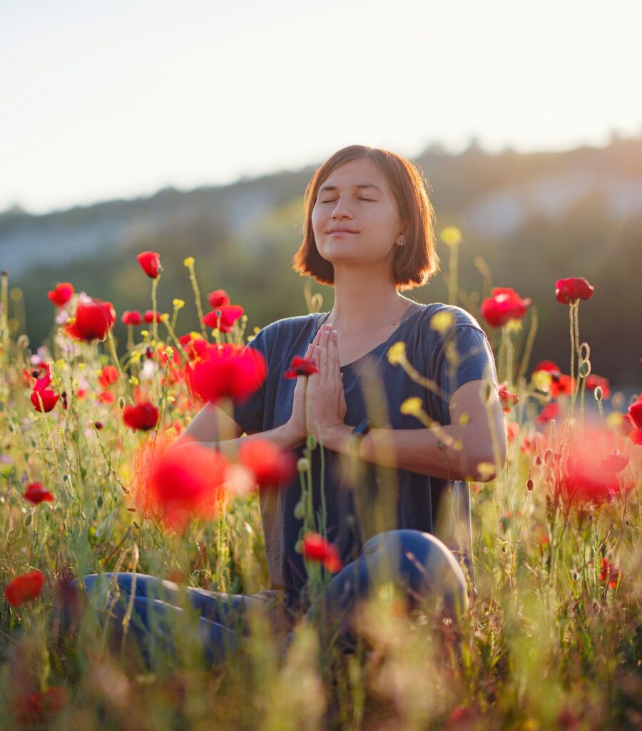 A beautiful woman meditates on a poppy field at sunset